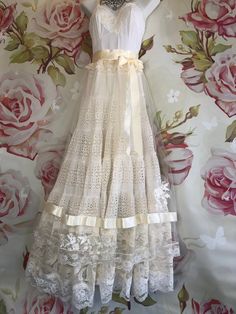 a white dress hanging on a wall with roses in the background and lace around it