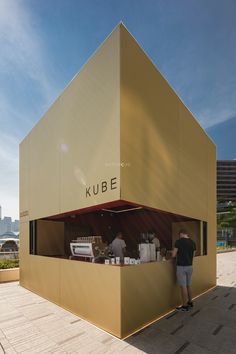 a man standing in front of a gold cube shaped building with people sitting at it