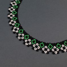 a black and green beaded necklace on a gray surface with white flowers in the center