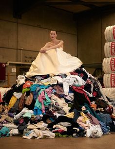 a woman is sitting on top of a pile of clothes in an industrial building,