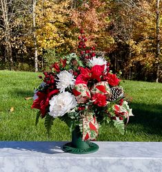 a bouquet of red and white flowers in a green vase on a table with trees in the background