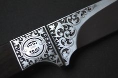 a knife that is sitting on top of a black surface with an ornate design around the blade