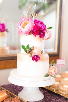 a white cake with pink flowers on top sitting on a table next to pastries