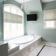 a large white bath tub sitting in a bathroom next to a tv mounted on the wall