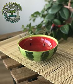 a green and red bowl sitting on top of a wooden table next to a potted plant