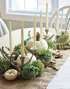 a table topped with candles and greenery next to a white vase filled with pumpkins