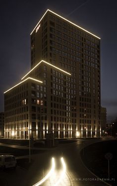 a very tall building lit up at night with lights on it's sides and cars driving down the street