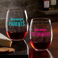 two wine glasses sitting on top of a wooden table next to cheese and crackers