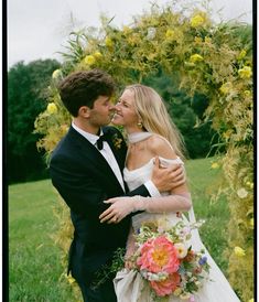 a bride and groom embracing each other in front of an arch with flowers on it