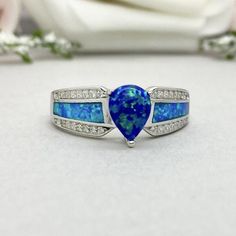 This beautiful ring is made from genuine 925 sterling silver with rhodium plating.Ring details--The Main stone is a pear shape 8mm by 6mm Lab Created Blue Opal Stone-Side stones are Round Clear 1mm simulated diamonds and Blue Lab Created Inlay Opal-Ring is casted in solid 925 sterling silver with rhodium plating (yellow gold and rose gold plated also available, please check the drop down menu for more options)-The Total face height of the ring measures 8mms and the band width measures 2.3mms-Eac Silver Teardrop Opal Promise Ring, Teardrop Opal Promise Ring In Fine Jewelry Style, Sterling Silver Pear-shaped Ring For Anniversary, Teardrop Opal Promise Ring Fine Jewelry, Sterling Silver Pear Shaped Ring For Anniversary, Pear Shaped Sterling Silver Anniversary Rings, Pear-shaped Sterling Silver Anniversary Ring, Fine Jewelry Teardrop Opal Ring For Anniversary, Sapphire Teardrop Sterling Silver Ring