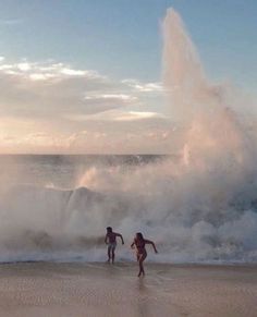 two people are playing in the water near an ocean wave that is crashing on them