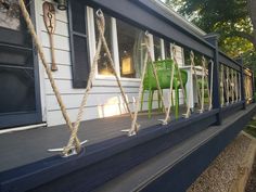 two green chairs sitting on top of a porch next to a white house with black shutters