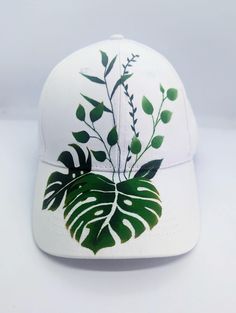 a white baseball cap with green leaves on the front and back side, sitting on a white surface