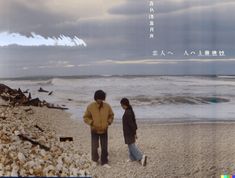 two people standing on the beach looking at the ocean