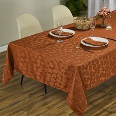 an orange table cloth with white plates and silverware sits on top of a wooden floor