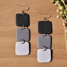 three square shaped earrings hanging from hooks on a wooden table next to a plant with green leaves