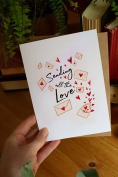 someone holding up a card that says sending all the love with envelopes and hearts