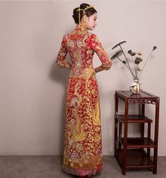 a woman in a red and gold dress standing next to a table with flowers on it