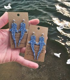 two small blue bird earrings with polka dots on them are being held in front of the water