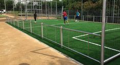 three people are playing soccer on a field with green grass and fenced in areas around them