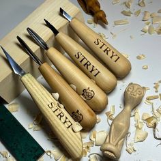 five wooden knives and carving tools on a table with wood shavings around them