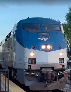 a blue and white train traveling down tracks next to a loading platform at a station