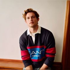 a young man sitting on top of a wooden bench in front of a mirror wearing a black and red sweater