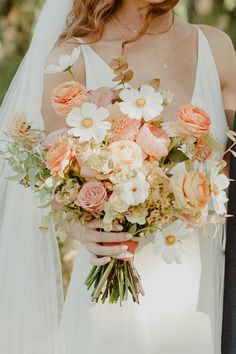 a bride holding a bouquet of peach and white flowers with her groom in the background