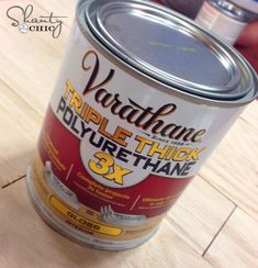 a can of paint sitting on top of a wooden table next to a person's hand