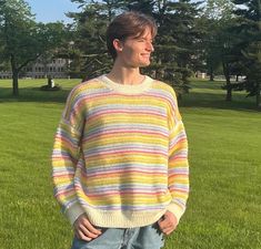 a man standing in the grass with his hands on his hips wearing a multicolored sweater