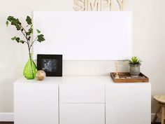 a white cabinet with some plants on top of it next to a sign that says simply