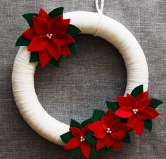 a white wreath decorated with red poinsettis and green leaves on a gray surface