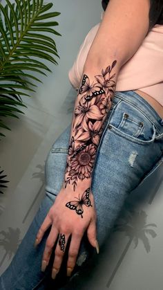 a woman's arm with flowers and butterflies tattooed on her left hand, sitting next to a plant