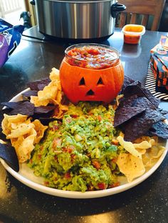 a white plate topped with guacamole, chips and a jack - o'- lantern