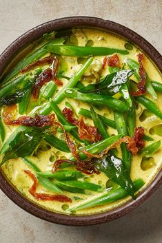 a brown bowl filled with green beans and bacon on top of a white countertop