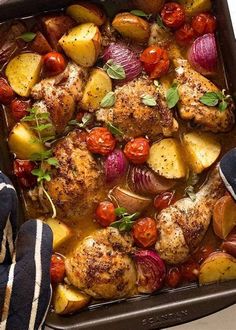 a pan filled with chicken, potatoes and tomatoes next to a pair of blue striped socks