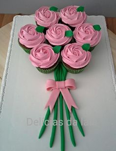 cupcakes with pink frosting and green stems are arranged on a white plate