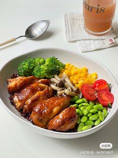 a white bowl filled with lots of food next to a glass of juice and spoon