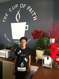 a woman standing in front of a cup of faith coffee shop counter with red flowers