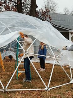 two people standing in front of a white structure with plastic covering it's sides