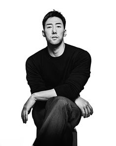 a black and white photo of a man with his arms crossed sitting on a suitcase