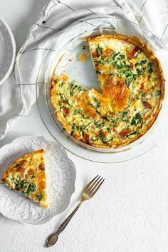 a cheese and spinach quiche on a white plate next to a slice missing