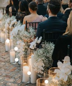 a row of chairs with candles and flowers on them in front of people sitting down