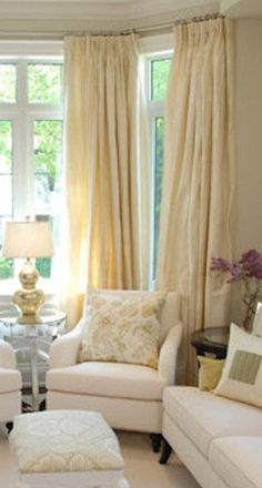 a living room filled with white furniture and windows covered in yellow drapes on top of them