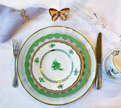 a table setting with green and gold plates, silverware and butterfly napkins on it