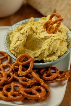 a bowl of hummus and pretzels on a plate with onion rings in the foreground