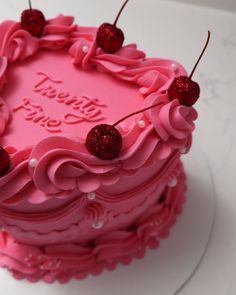 a pink birthday cake with cherries on top