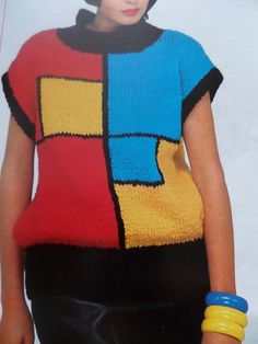 a woman wearing a multicolored sweater with black pants and yellow bracelets stands in front of a white background