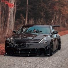 a black sports car parked on the side of a road in front of some trees