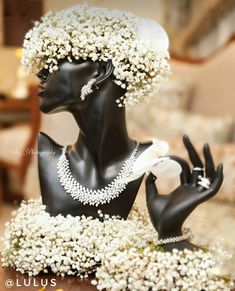 a black mannequin with white flowers and pearls on it's head, sitting on a table